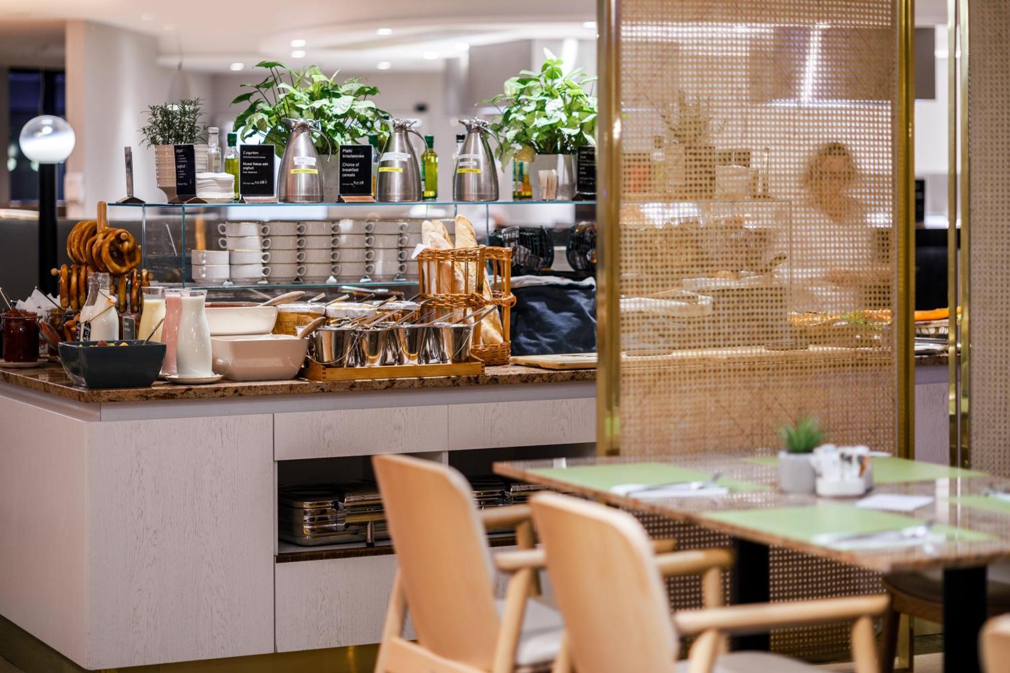 Radisson Blu Resort Świnoujście Екстериор снимка The photo shows a modern café or dining area. In the foreground, there are wooden chairs and tables set up for dining. In the background, there is a display counter with various items, including plants in pots, containers, and possibly dishes or uten