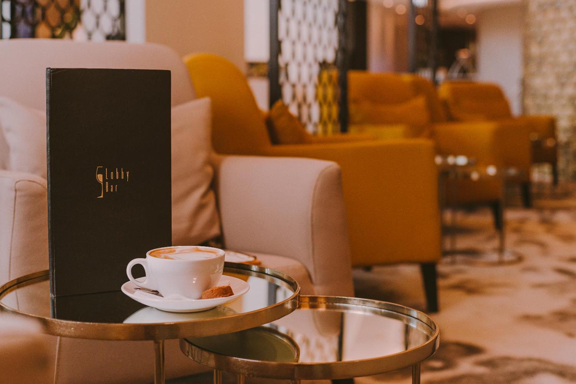 Radisson Blu Resort Świnoujście Екстериор снимка The photo shows a cozy indoor setting with a stylish, modern atmosphere. In the foreground, there is a small round glass table with a white coffee cup and a saucer, alongside a small biscuit or cookie. Next to the coffee, there is a black menu with e