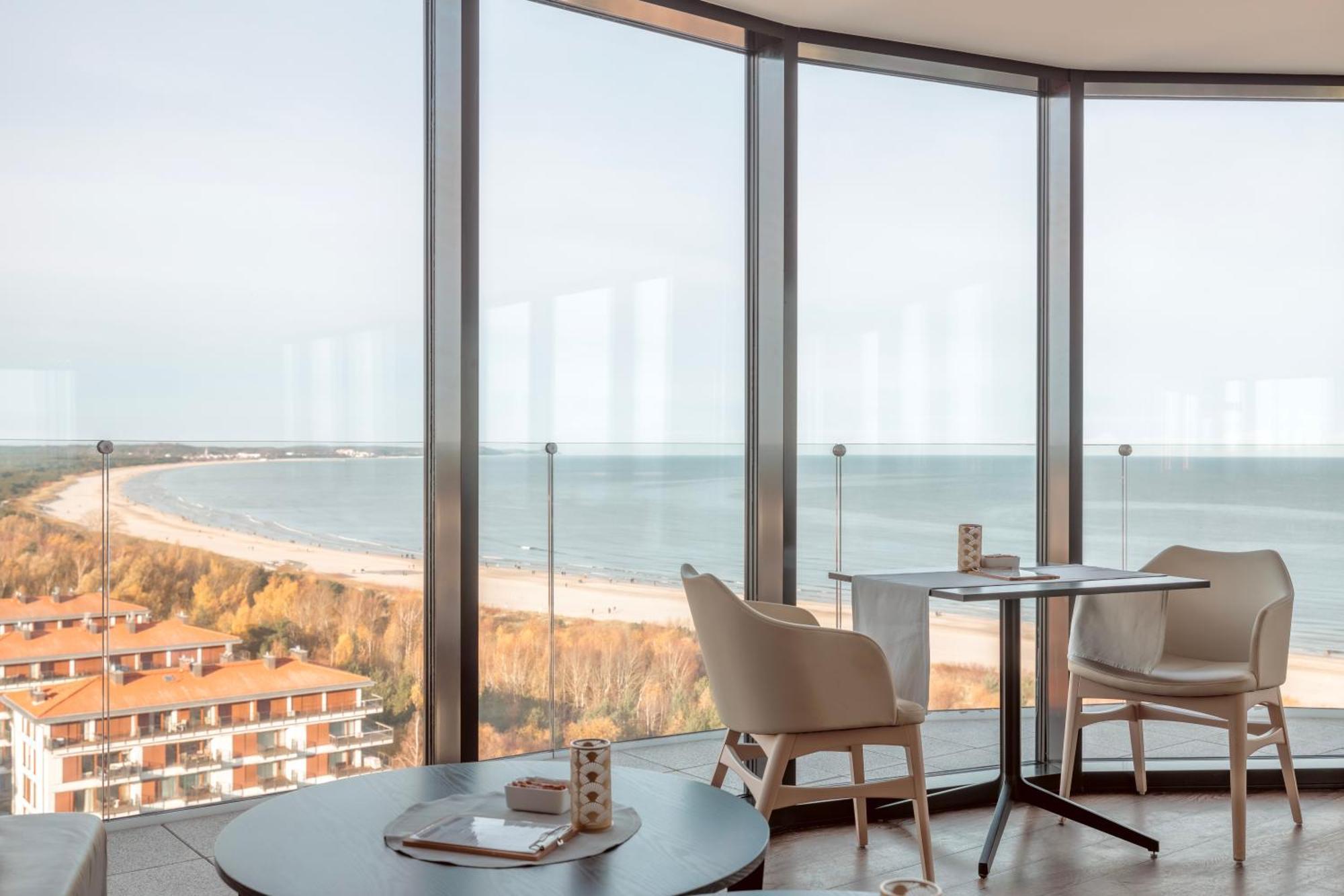 Radisson Blu Resort Świnoujście Екстериор снимка The photo shows a modern interior space with large floor-to-ceiling windows that provide a stunning view of the beach and sea. The area appears to be a dining or lounge space, featuring a minimalistic table and chairs. There is a sense of tranquility