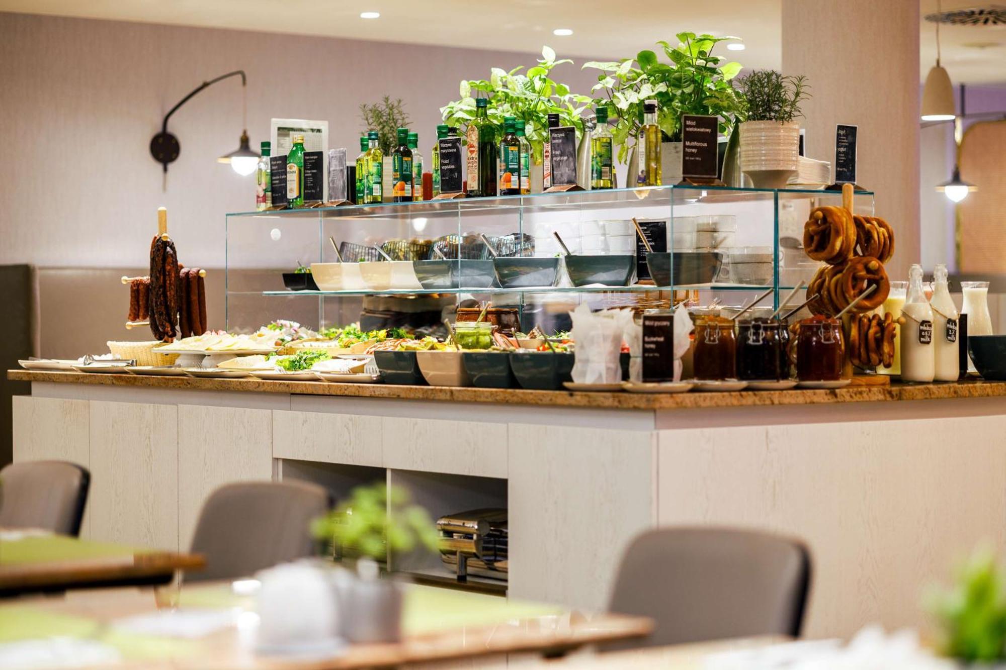 Radisson Blu Resort Świnoujście Екстериор снимка The photo shows a well-organized buffet display in a restaurant setting. There is a glass counter filled with various dishes. On the upper shelf, there are several bottles of oil and herbs, indicating a focus on fresh and healthy ingredients. Below t