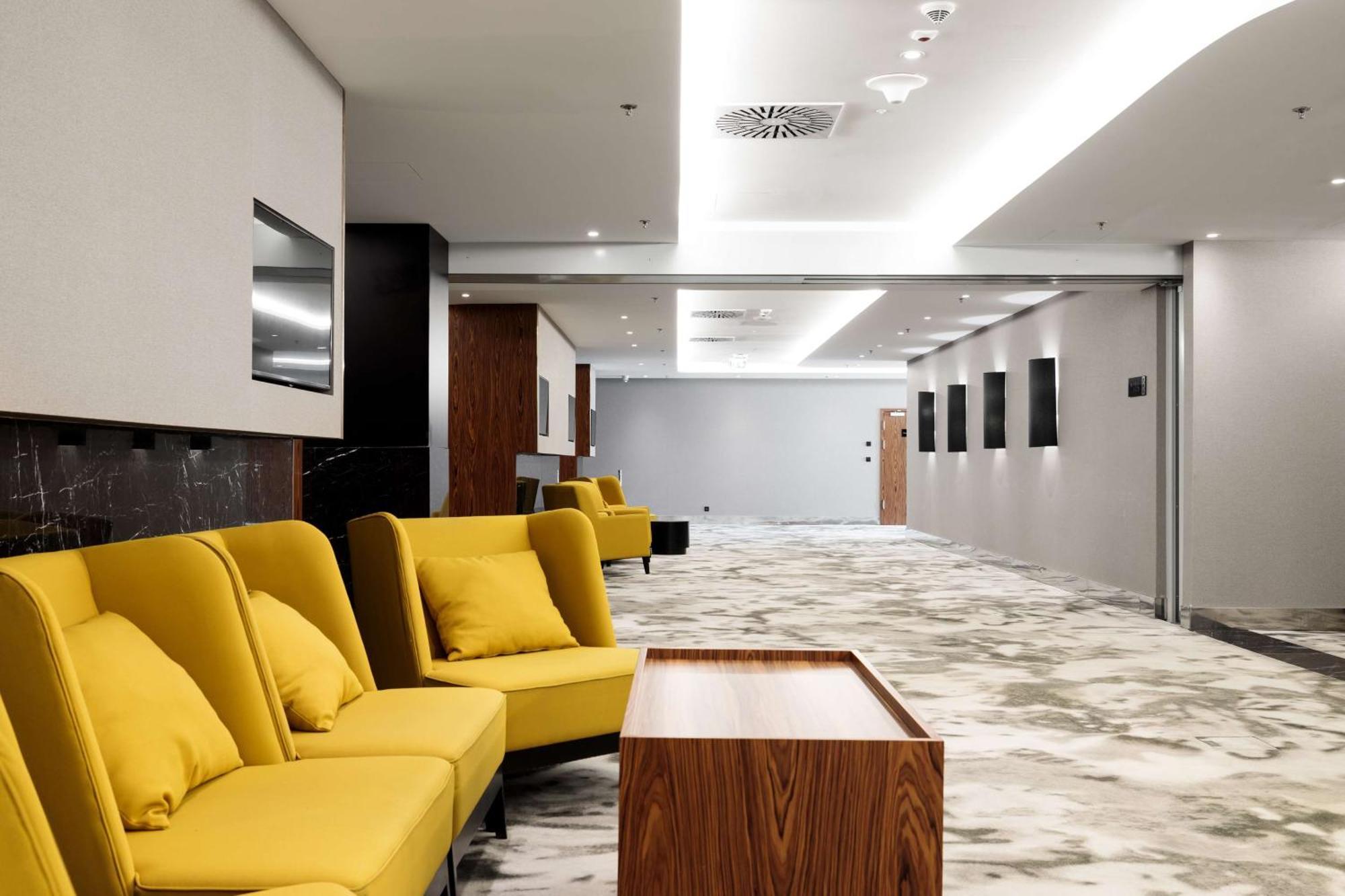 Radisson Blu Resort Świnoujście Екстериор снимка The photo shows a modern interior space, likely a lobby or waiting area. There are several yellow sofas with cushions arranged in a casual seating area. In front of the sofas, there is a wooden coffee table. The flooring features a gray and white mar