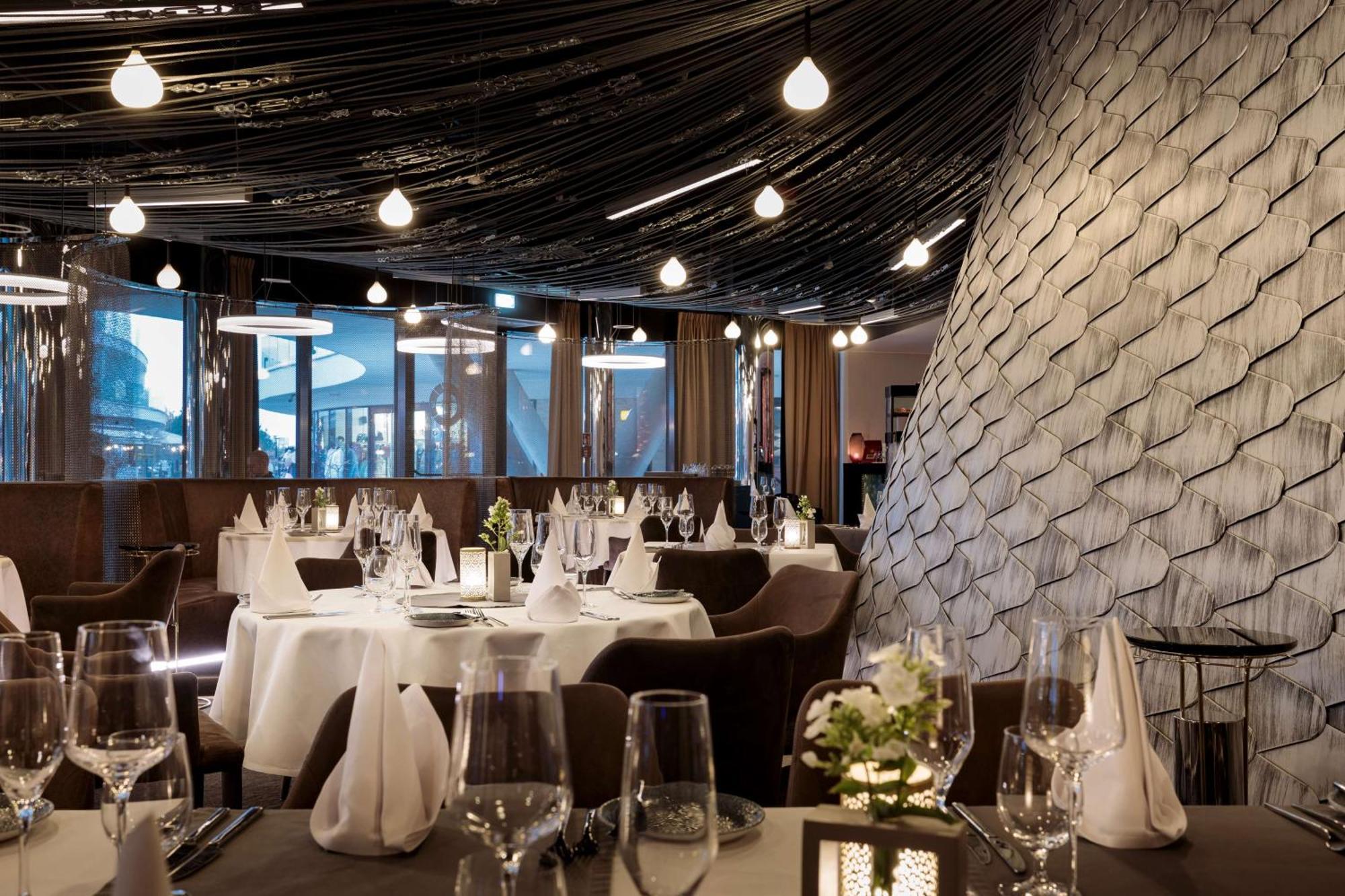 Radisson Blu Resort Świnoujście Екстериор снимка The photo shows a stylish restaurant interior. The dining area features elegantly set tables with white tablecloths, glassware, and folded napkins. There are decorative elements like small floral arrangements on the tables. The ceiling is adorned wit