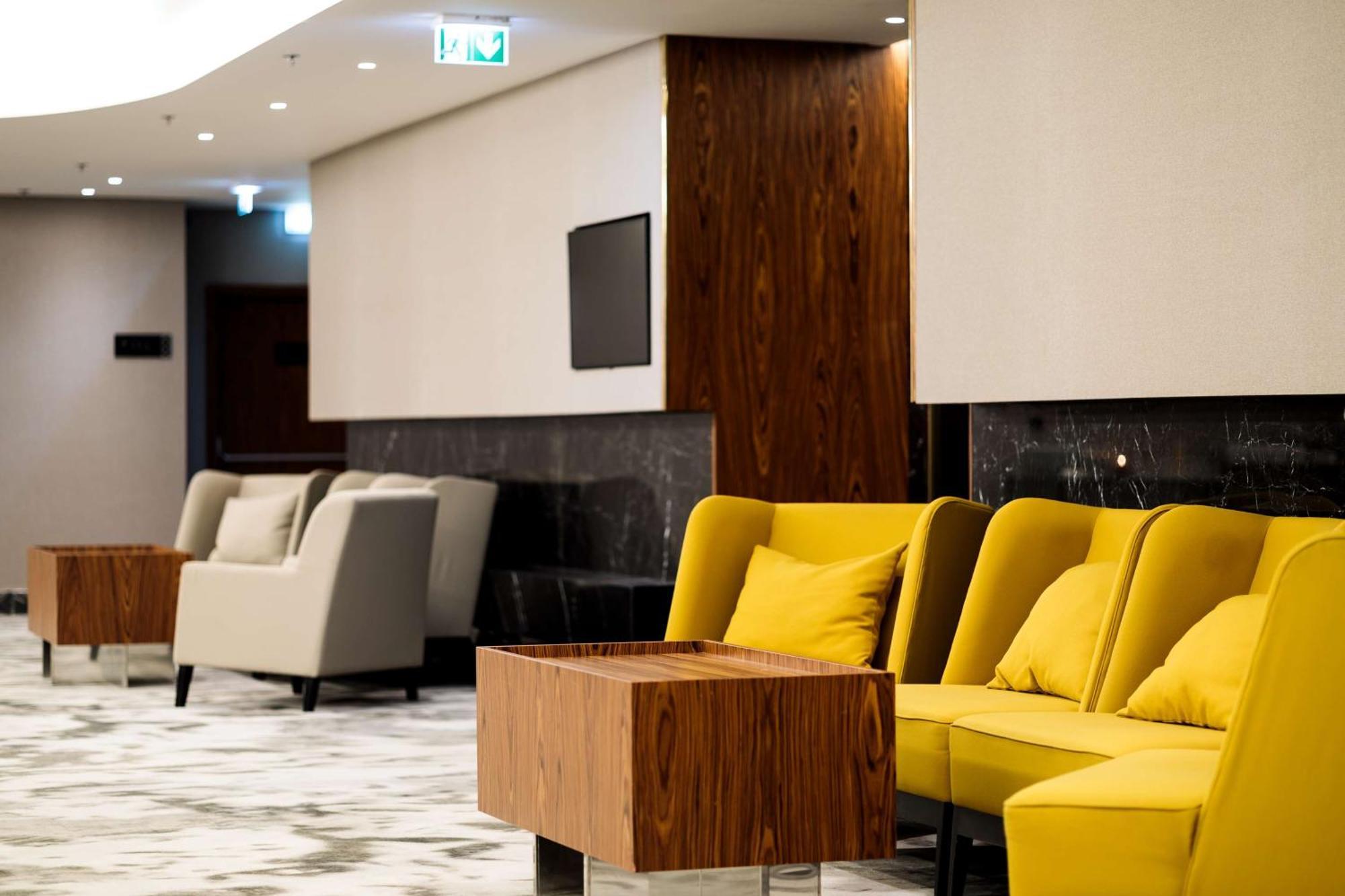 Radisson Blu Resort Świnoujście Екстериор снимка The photo depicts a modern lounge or waiting area with stylish seating. On the left, there are soft gray armchairs arranged around a wooden coffee table. In the center, there are yellow chairs with plush cushions, contributing a vibrant contrast to t