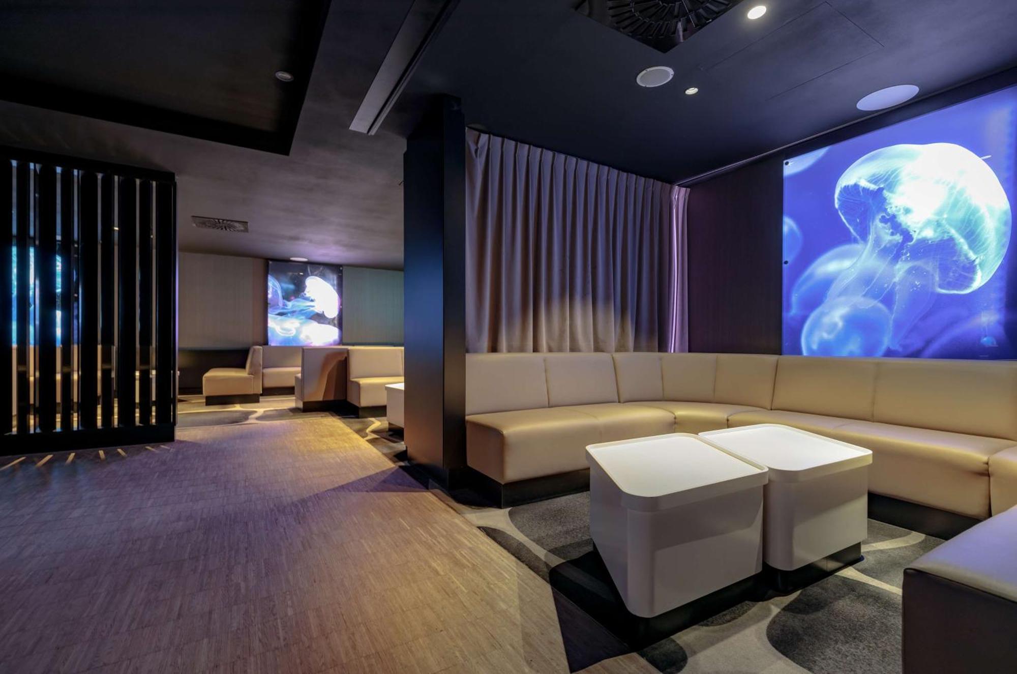 Radisson Blu Resort Świnoujście Екстериор снимка The photo shows a modern interior space that appears to be a lounge or relaxation area. The design is sleek and minimalist, featuring a curved, light-colored seating arrangement with low tables at the center. The walls are dark, contributing to a coz