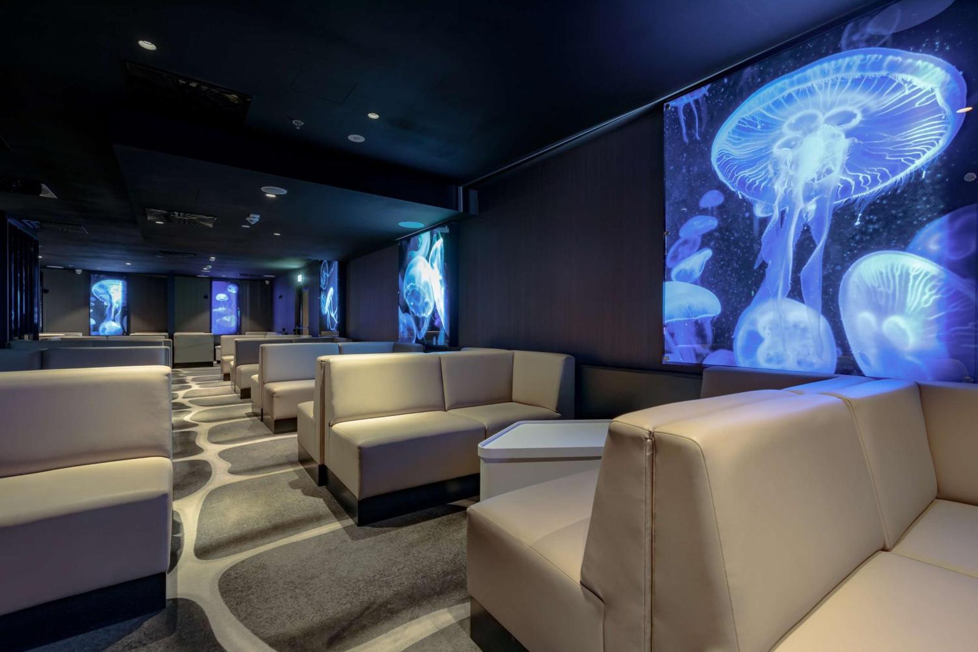 Radisson Blu Resort Świnoujście Екстериор снимка The photo shows a modern lounge space with a sleek design. The area features light-colored, upholstered seating arranged in an open layout. The walls are decorated with large, vibrant images of jellyfish illuminated in blue, creating a calming underw