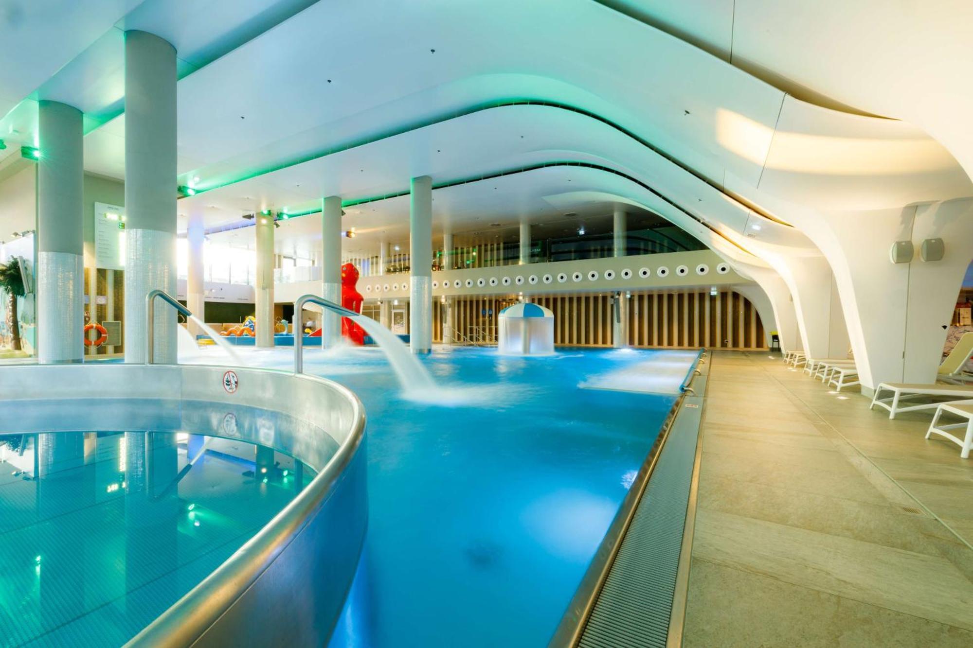 Radisson Blu Resort Świnoujście Екстериор снимка The photo shows a modern indoor swimming pool area with an elegant design. The pool features curved edges and is filled with clear, blue water. There are various amenities, such as jets for relaxation and possibly seating areas along the edges. The l