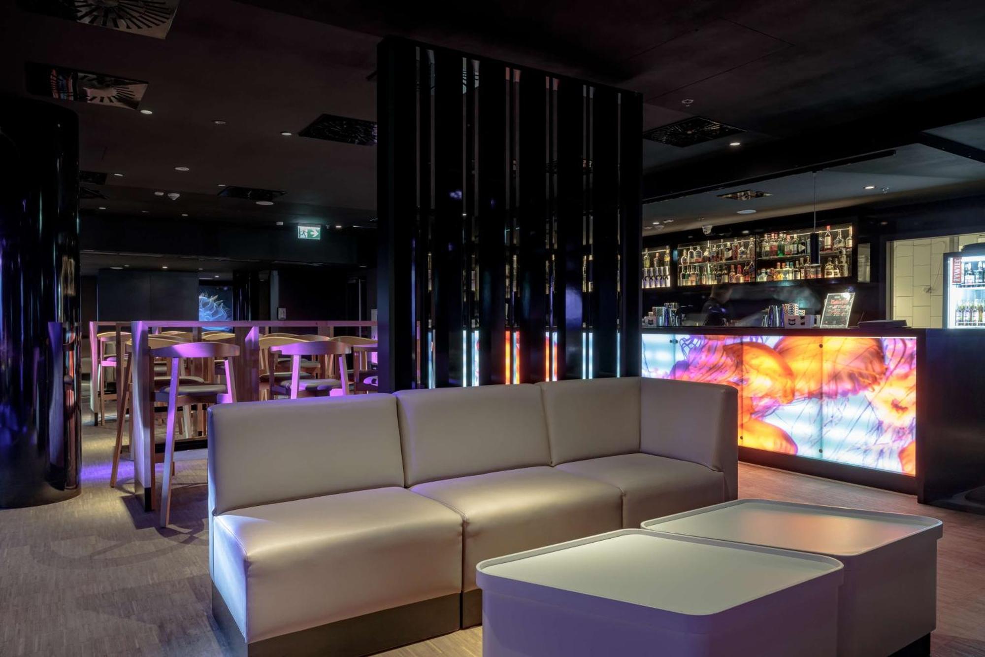 Radisson Blu Resort Świnoujście Екстериор снимка The photo depicts a modern interior space, possibly a lounge or bar. There are sleek, minimalistic furniture pieces, including a large, curved sofa and contemporary coffee tables. The lighting is dim, with a blend of colorful ambient lights illuminat