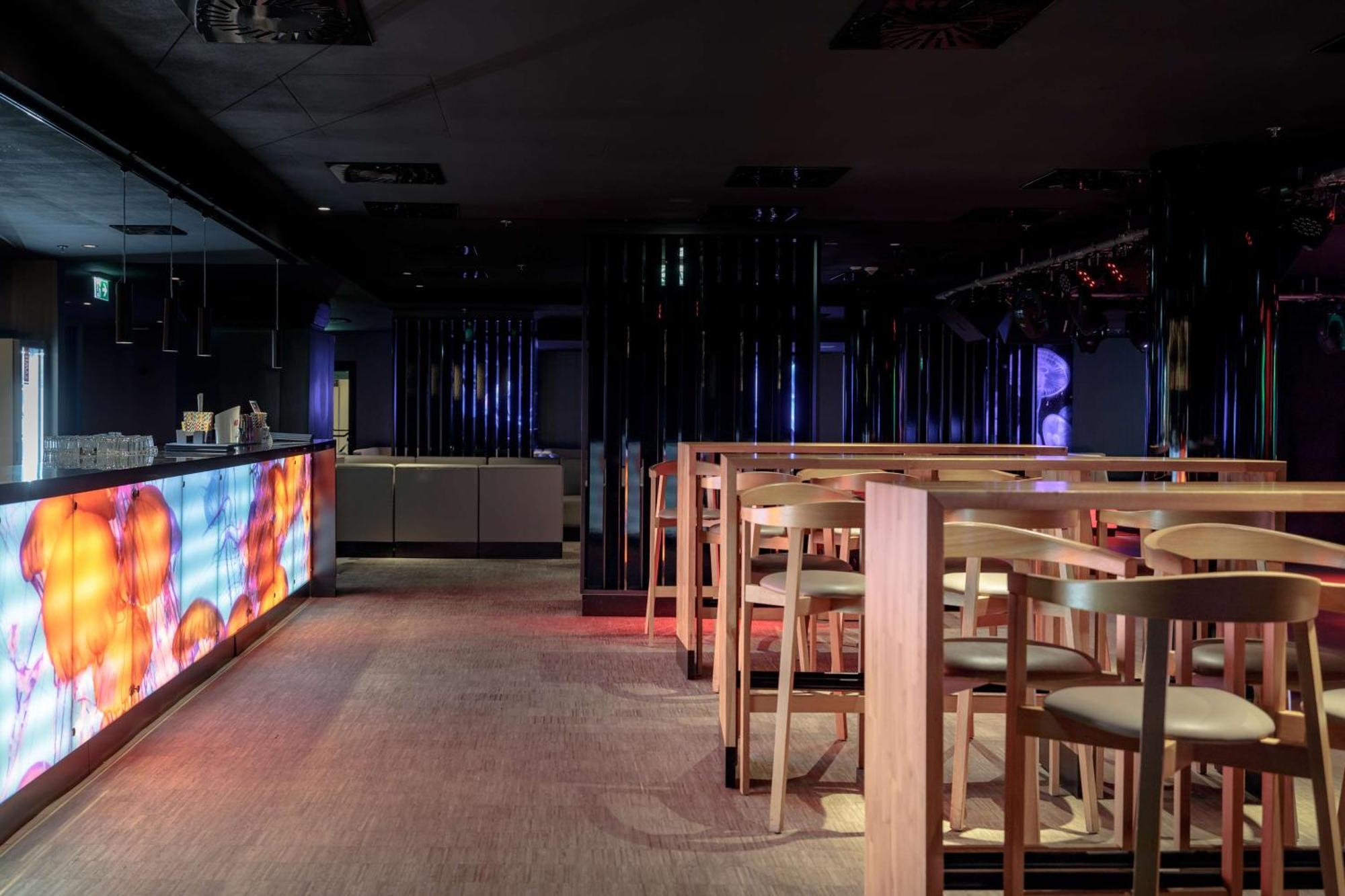 Radisson Blu Resort Świnoujście Екстериор снимка The photo shows the interior of a modern bar or nightclub. It features a sleek and stylish design with a long bar counter illuminated by colorful lights. The floor has a neutral carpet, and there are wooden high-top tables with accompanying chairs ar