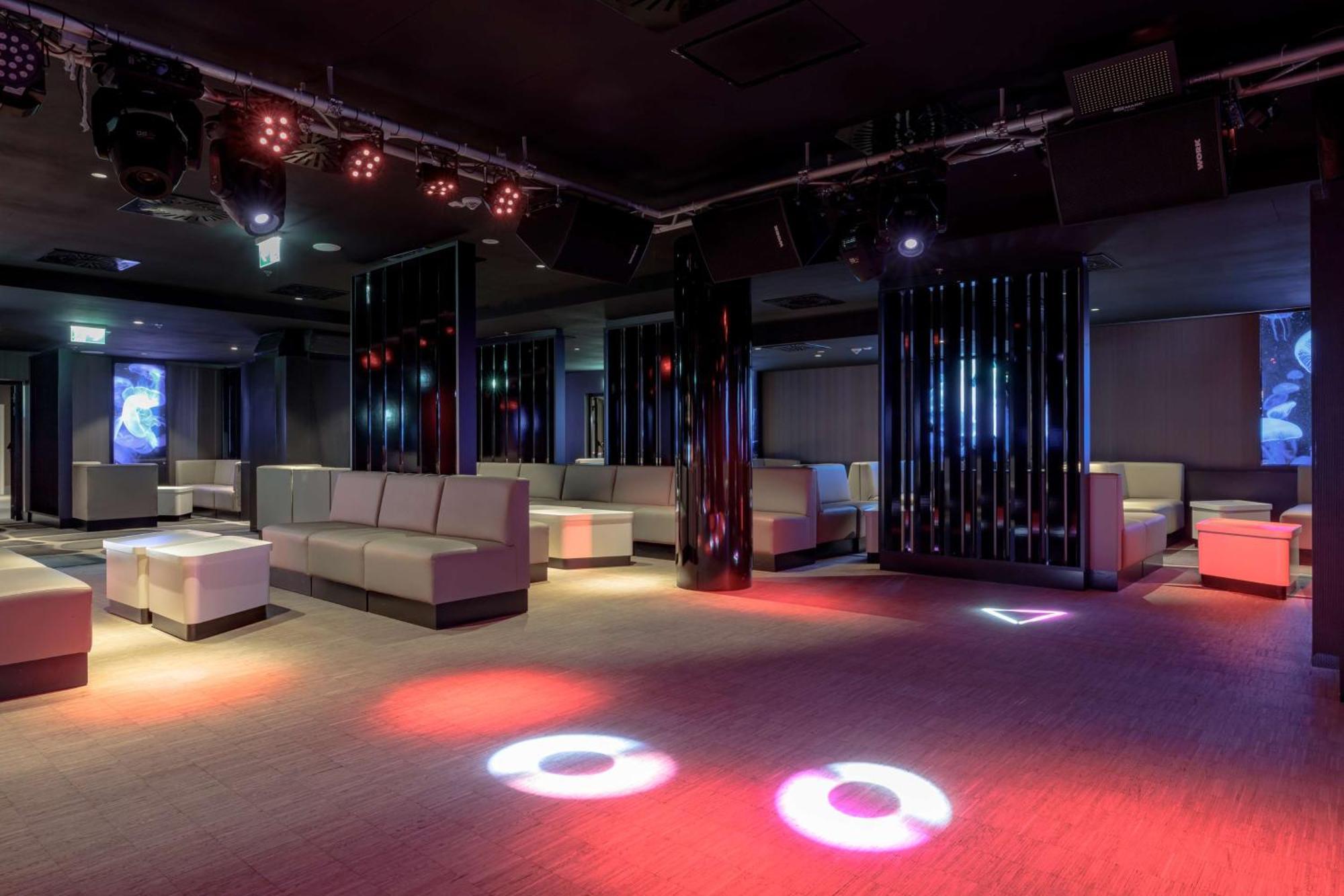 Radisson Blu Resort Świnoujście Екстериор снимка The photo depicts a modern nightclub interior, featuring a spacious layout with sleek, minimalist seating arrangements. The room has plush seating along the walls, and the floor is illuminated with circular lights in varying colors, creating a vibran