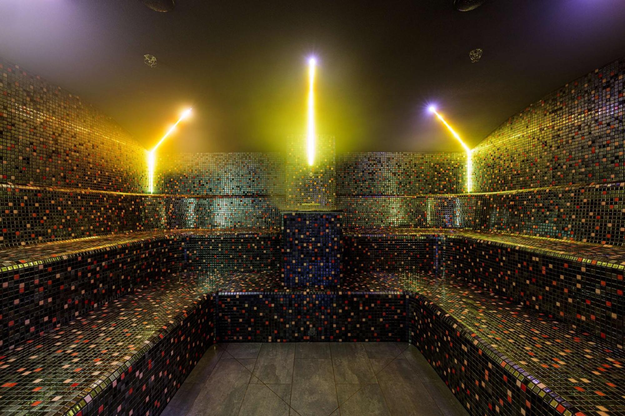 Radisson Blu Resort Świnoujście Екстериор снимка The photo shows the interior of a steam room or sauna. The space is characterized by a series of benches that are built into the walls, allowing for multiple seating options. The walls are adorned with a mosaic of small, colorful tiles that create a 