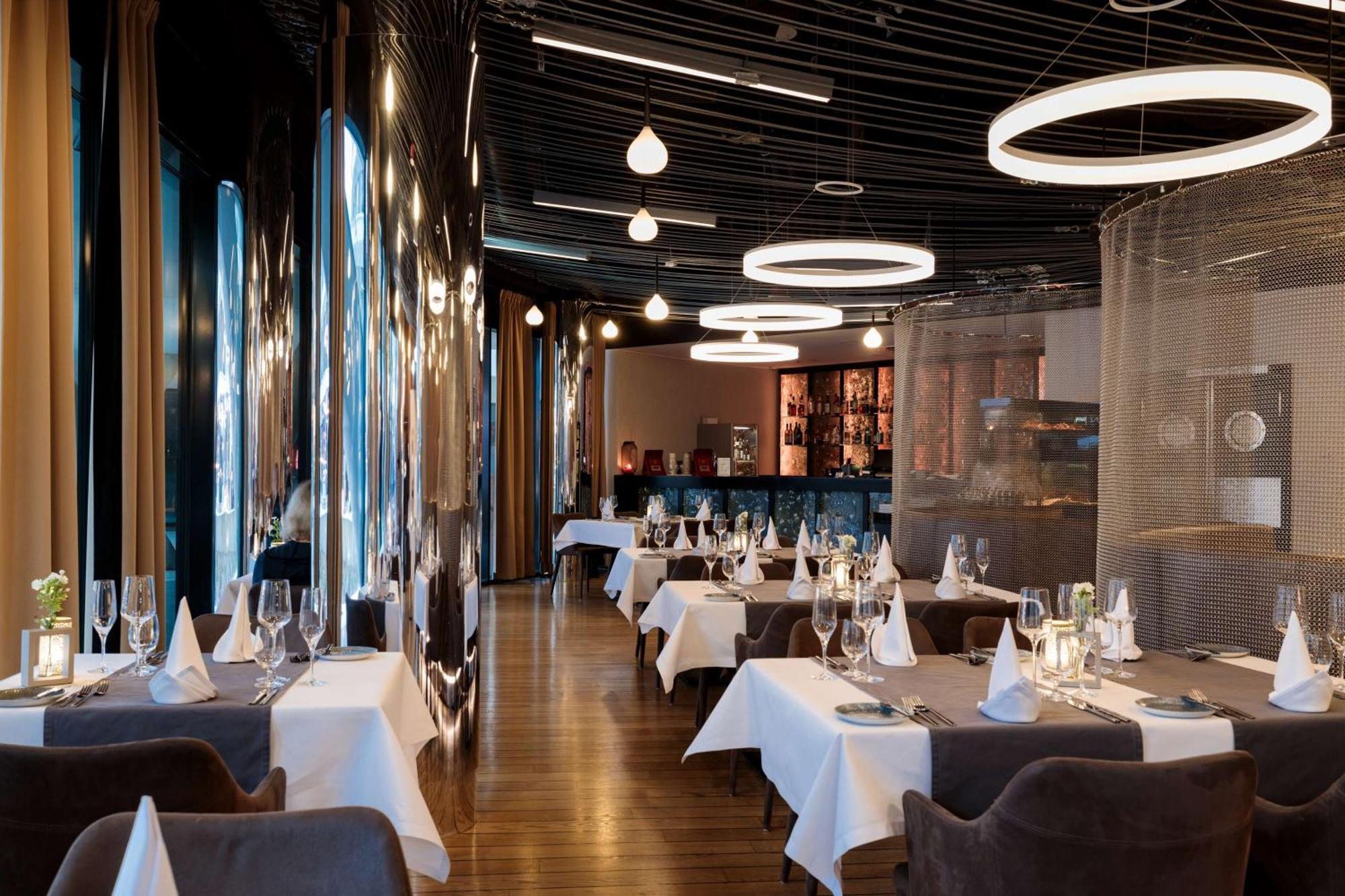 Radisson Blu Resort Świnoujście Екстериор снимка The photo shows the interior of a modern restaurant. It features elegantly set tables with white tablecloths and neatly arranged glassware. The design includes a sleek, contemporary aesthetic with dark walls and interesting lighting, including circul