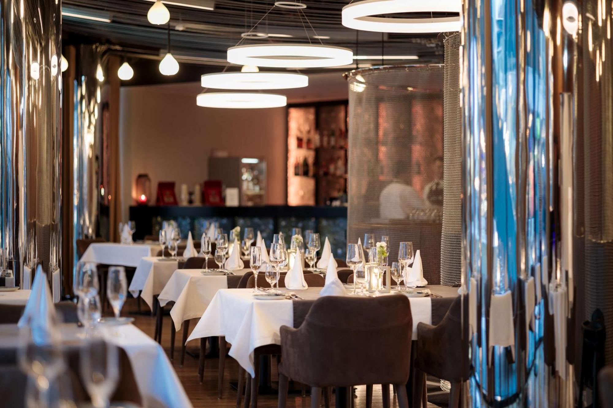 Radisson Blu Resort Świnoujście Екстериор снимка The photo depicts an elegant restaurant interior. There are several tables covered with white tablecloths, each set with glassware and napkins, suggesting a fine dining experience. The chairs are upholstered, providing a comfortable seating arrangeme
