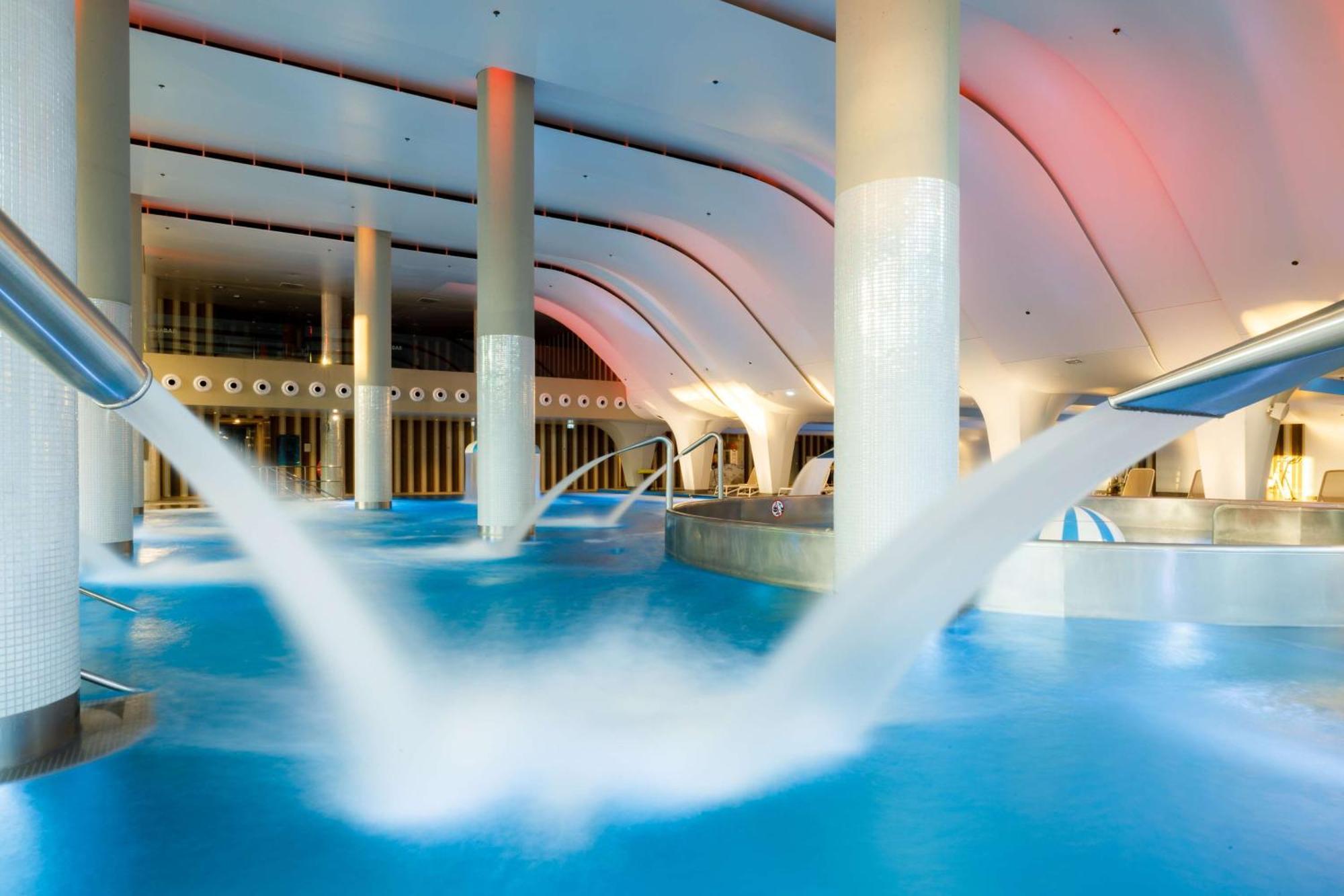 Radisson Blu Resort Świnoujście Екстериор снимка The photo depicts an indoor swimming pool area characterized by modern architecture. The pool is filled with clear blue water, and there are several columns supporting the ceiling. Water features, such as jets or fountains, are seen creating flowing 