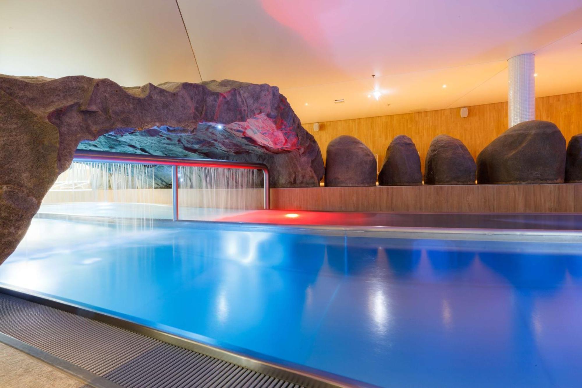 Radisson Blu Resort Świnoujście Екстериор снимка The photo shows a serene indoor swimming pool area. The pool has clear blue water, and there is a distinctive rock formation that resembles a cave on one side. Soft lighting enhances the atmosphere, casting a gentle glow across the space. In the back