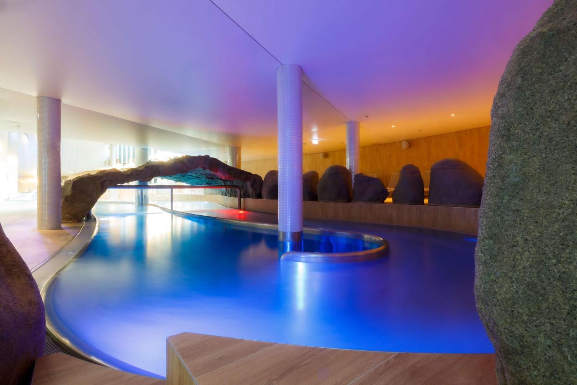 Radisson Blu Resort Świnoujście Екстериор снимка The photo showcases an elegant indoor swimming pool area. The pool has a flowing, organic shape and is illuminated with soft blue and purple lighting, creating a calming ambiance. Surrounding the pool are smooth, natural-looking stones and wooden ele