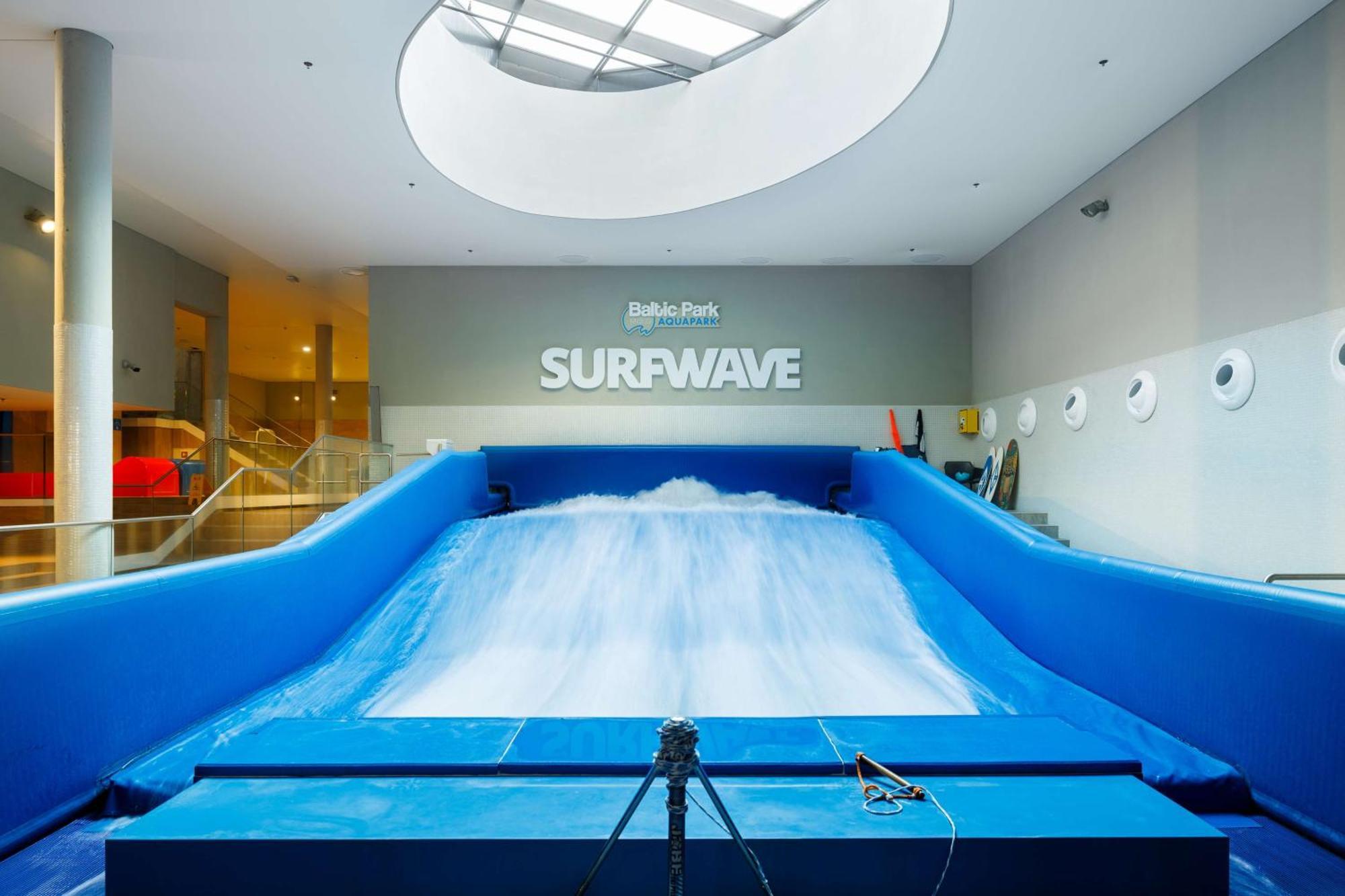 Radisson Blu Resort Świnoujście Екстериор снимка The photo shows an indoor surfing attraction called "Surfwave." It features a large blue ramp with water flowing down it, creating a wave-like effect for surfing. Above the ramp, there is a sign that says "SURFWAVE." The area appears well-lit and mod